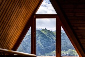 Une fenêtre triangulaire offrant une vue sur un paysage montagneux et un petit bâtiment situé sur une colline.