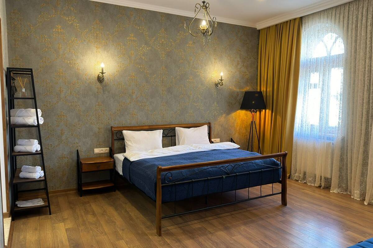 Ein ordentlich eingerichtetes Schlafzimmer mit einem hölzernen Bett, einem Nachttisch, einer Lampe und einem Regal mit Handtüchern.