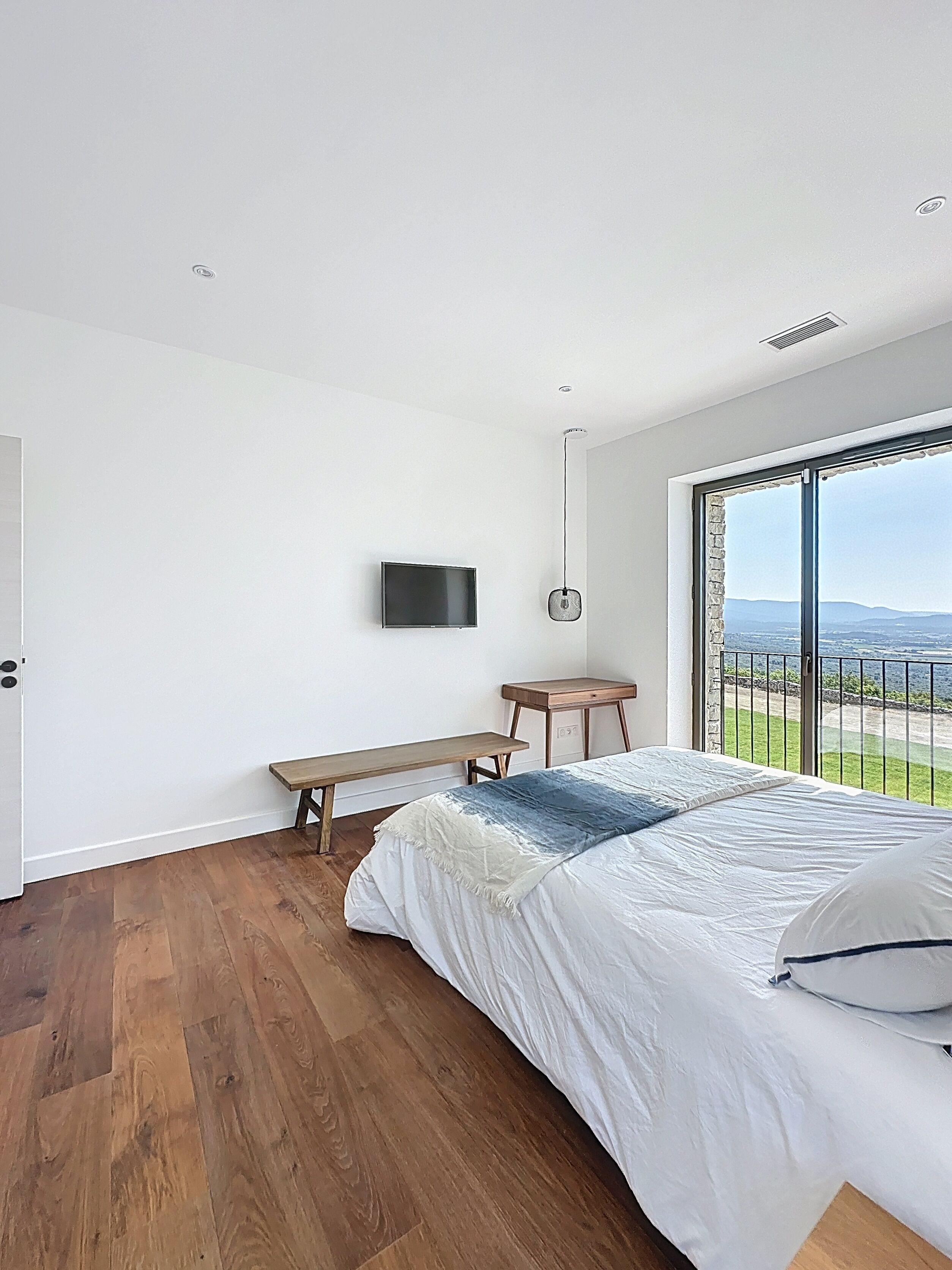 Ein Schlafzimmer mit einem großen Bett, einem an der Wand montierten Fernseher, einem kleinen Tisch und einer Bank.