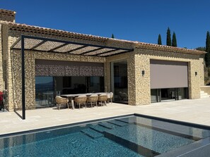 A poolside area with a stone exterior, a covered patio, and a clear view of the pool.