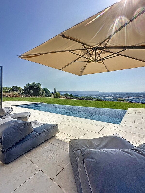 An outdoor pool area with a view of the landscape, a large umbrella, and modern outdoor furniture.