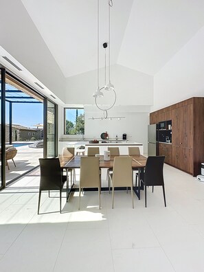 A modern kitchen with a dining area, large windows, and a view of the outdoors.