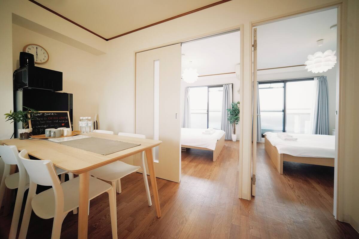 Una habitación de hotel moderna con piso de madera, un área de comedor con mesa y sillas, una cama y un ventanal grande.