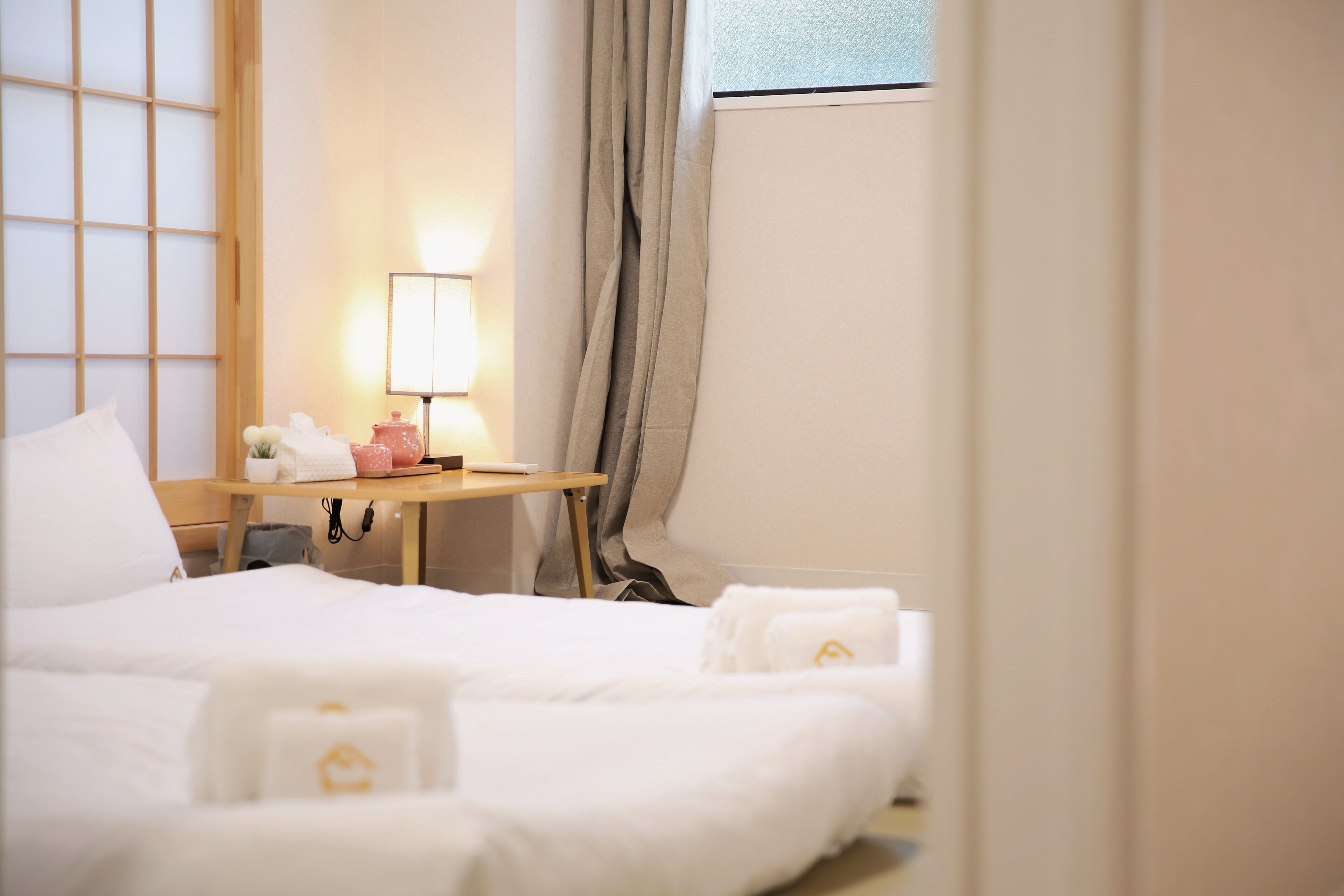 A hotel room with a bed, a bedside table with a lamp, a window with curtains, and a view of the outside.