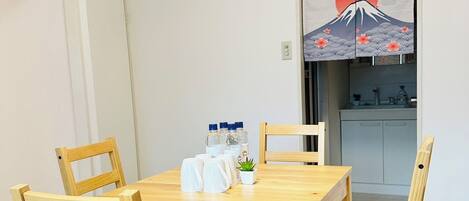 A dining area with a wooden table and chairs, a small potted plant, and a wall-mounted artwork depicting a mountain and sun.