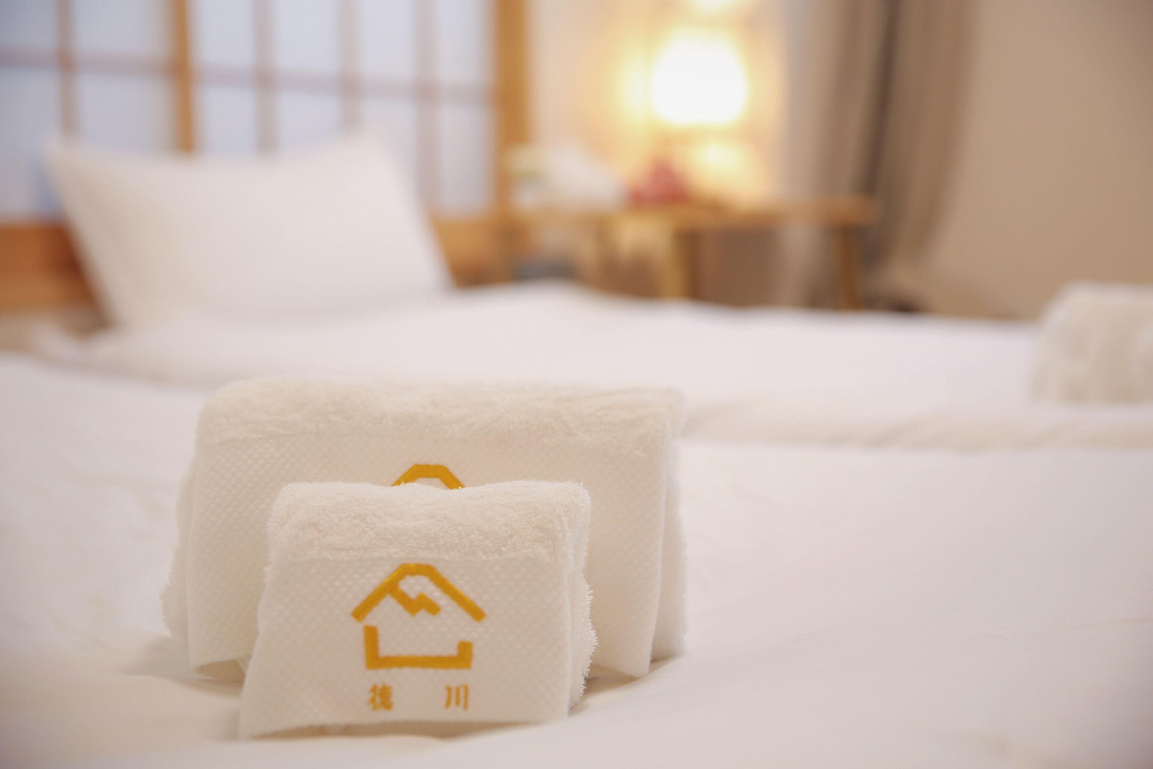 Een opgemaakt bed met witte lakens en twee handdoeken met een hotel logo.