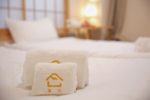 A neatly made bed with white linens and two towels with a hotel logo. - CU Host CASA (Osaka)