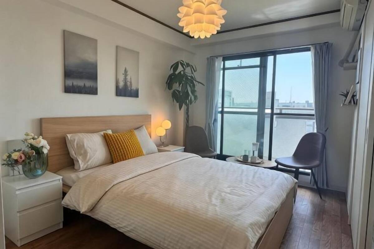 Una habitación de hotel con cama, mesitas de noche, una ventana con vistas y una planta.