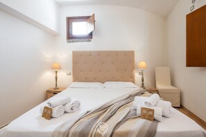 A hotel room with a large bed, two bedside tables with lamps, a chair, and a small window. - Cliffside Blue - Costa Rei (Muravera)