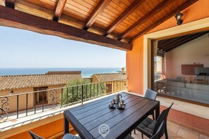 A balcony with a wooden table and chairs, a view of the sea, and a glass door leading to an indoor area. - Cliffside Blue - Costa Rei (Muravera)