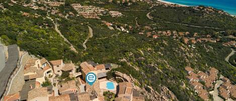 An aerial view of a coastal village with terraced houses, a beach, and a clear blue sea.