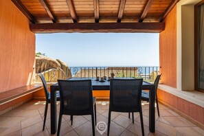Ein Balkon mit Holzboden, zwei schwarzen Korbstühlen und einem Tisch mit Teekanne und Tassen.