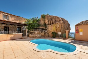 Ein Pool mit ungewöhnlicher Form, umgeben von einer Steinterrasse und einer großen Felsformation.