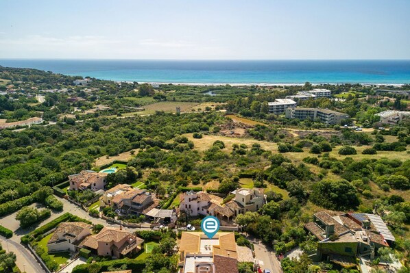 Vista aérea de una zona residencial costera con casas, piscina y vista al mar.