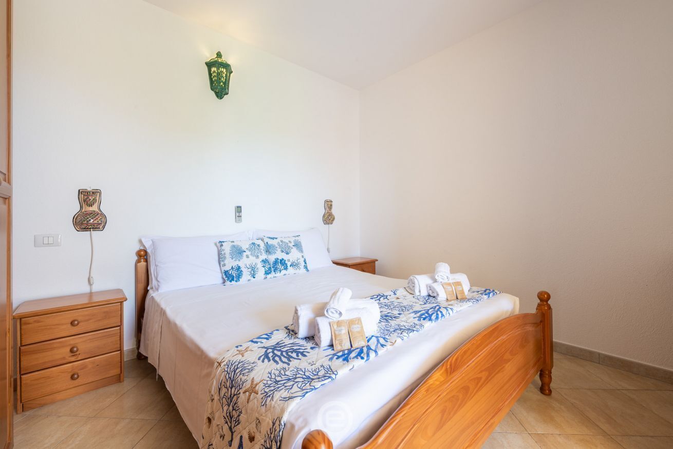 A neatly made bed with a floral bedspread, two bedside tables, and a wall-mounted light fixture.