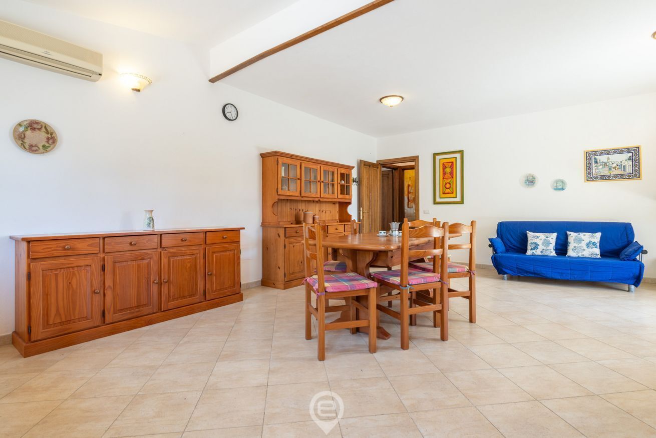 A spacious living area with a dining table, chairs, a blue sofa, wooden cabinets, and a kitchen area.