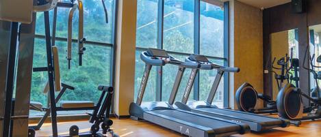 A gym with treadmills, weight machines, and a large window offering a view of greenery.
