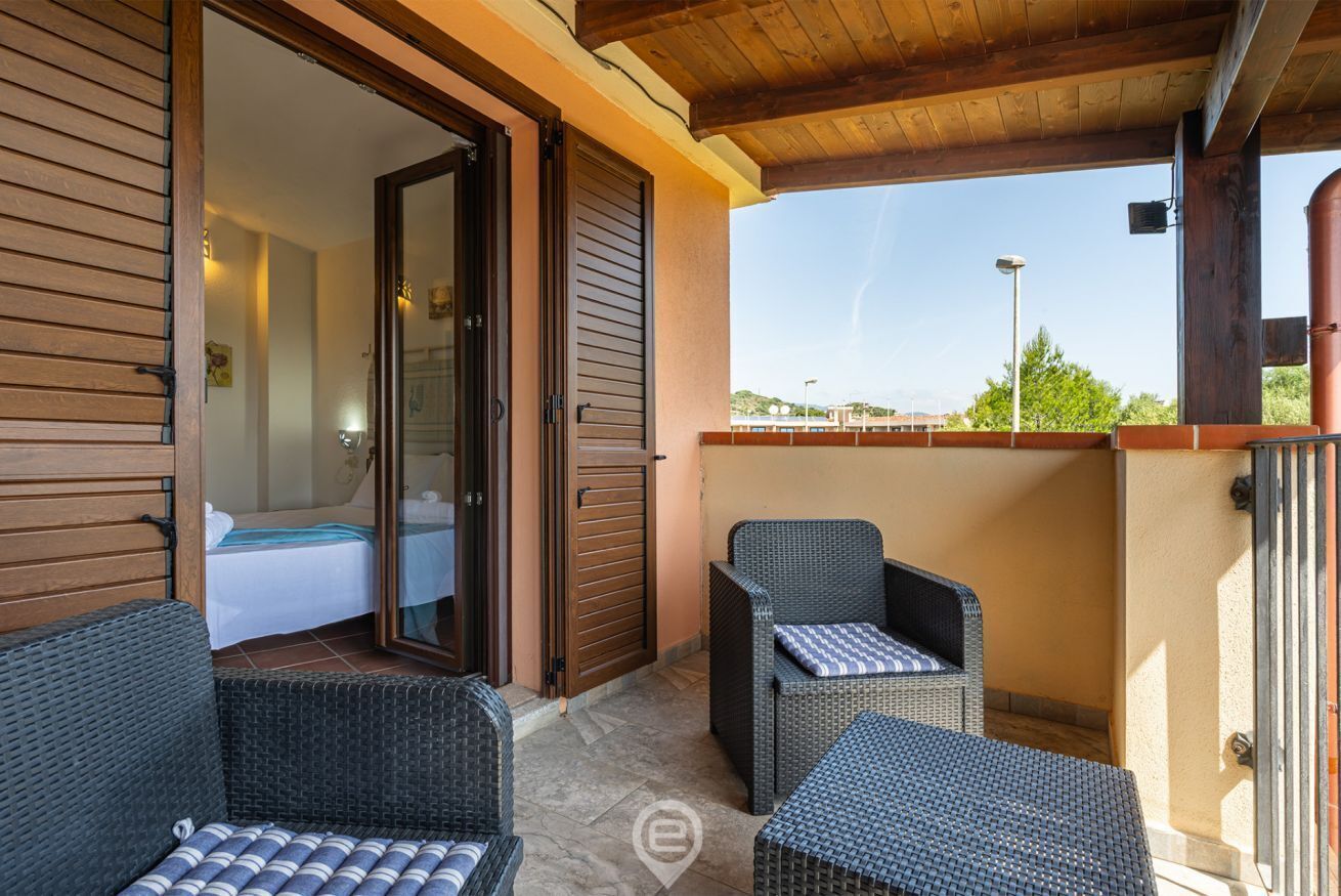 Ein Balkon mit Korbmöbeln, eine Schiebetür zum Schlafzimmer und freier Blick auf die Landschaft.