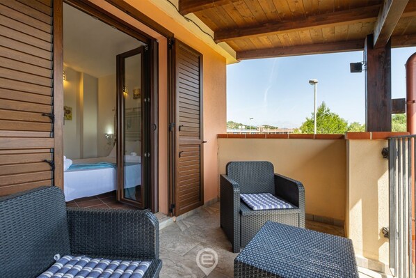 A balcony with wicker furniture, a sliding glass door leading to a bedroom, and a clear view of the landscape.