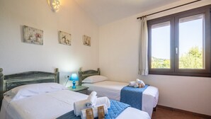 Une chambre d’hôtel avec deux lits, une fenêtre avec des rideaux, une lampe fixée au mur et trois tableaux encadrés.