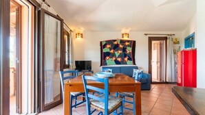 Un coin repas avec une table en bois et des chaises bleues, un canapé bleu, un réfrigérateur rouge et une courtepointe à motifs accrochée au mur.