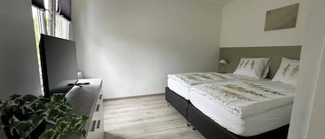 A bedroom with a bed, a desk, a TV, and a plant.