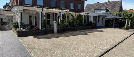 A building with a covered outdoor area, a parking sign, and a paved entrance.