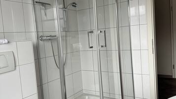 A modern bathroom with a glass-enclosed shower, a white toilet, and a wooden floor.