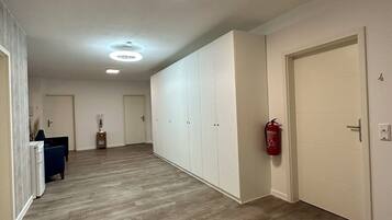 A hallway with wooden flooring, white walls, and a fire extinguisher mounted on the wall.