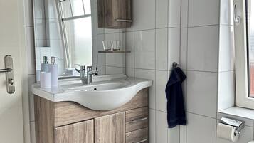 A modern bathroom with a wooden vanity, white tiles, a large mirror, and a towel hanging on the wall.