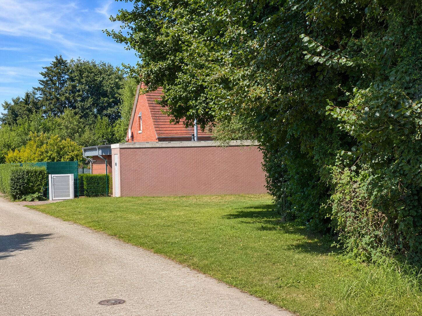 A paved driveway leading to a brick building with a red roof, surrounded by green grass and trees.