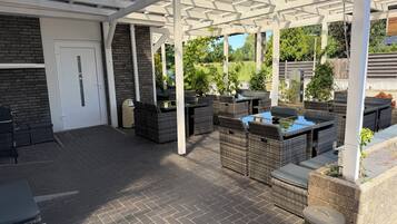 Een overdekt terras met tuinmeubilair, een deur en een vuilnisbak.