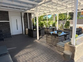 A covered patio area with outdoor furniture, a door, and a trash can.