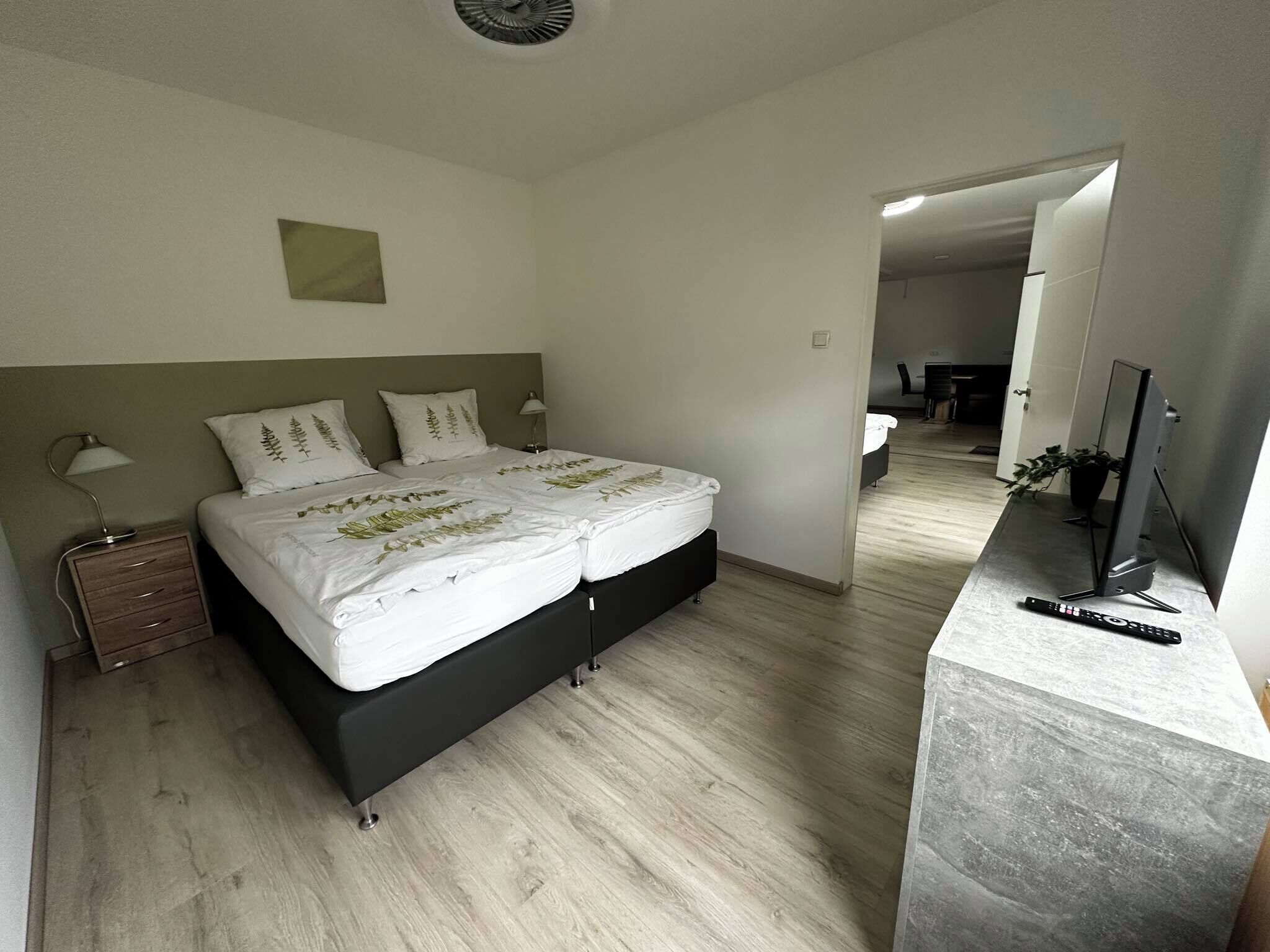 A modern bedroom with a bed, bedside tables, a desk, and a TV.