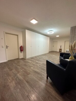 A spacious room with a wooden floor, a large wardrobe, a fire extinguisher, and a seating area with a vase. - Haus Wijnen (Bad Bentheim)