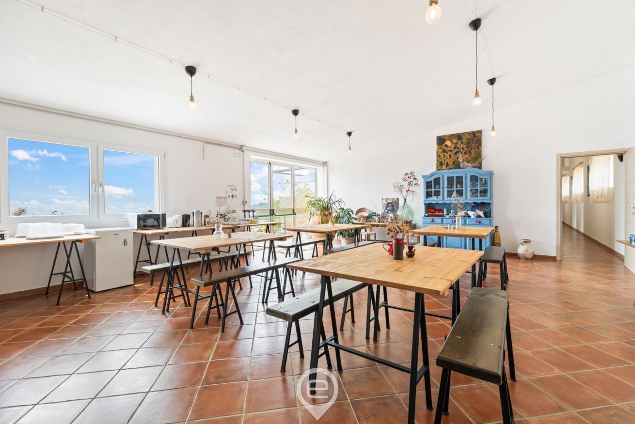 Une pièce spacieuse avec plusieurs tables et des bancs, de grandes fenêtres et un buffet bleu orné d’objets décoratifs.
