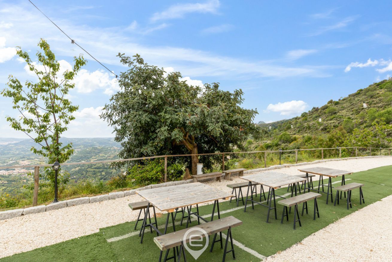 Een terras met tafels en banken, omgeven door groen en een prachtig uitzicht.