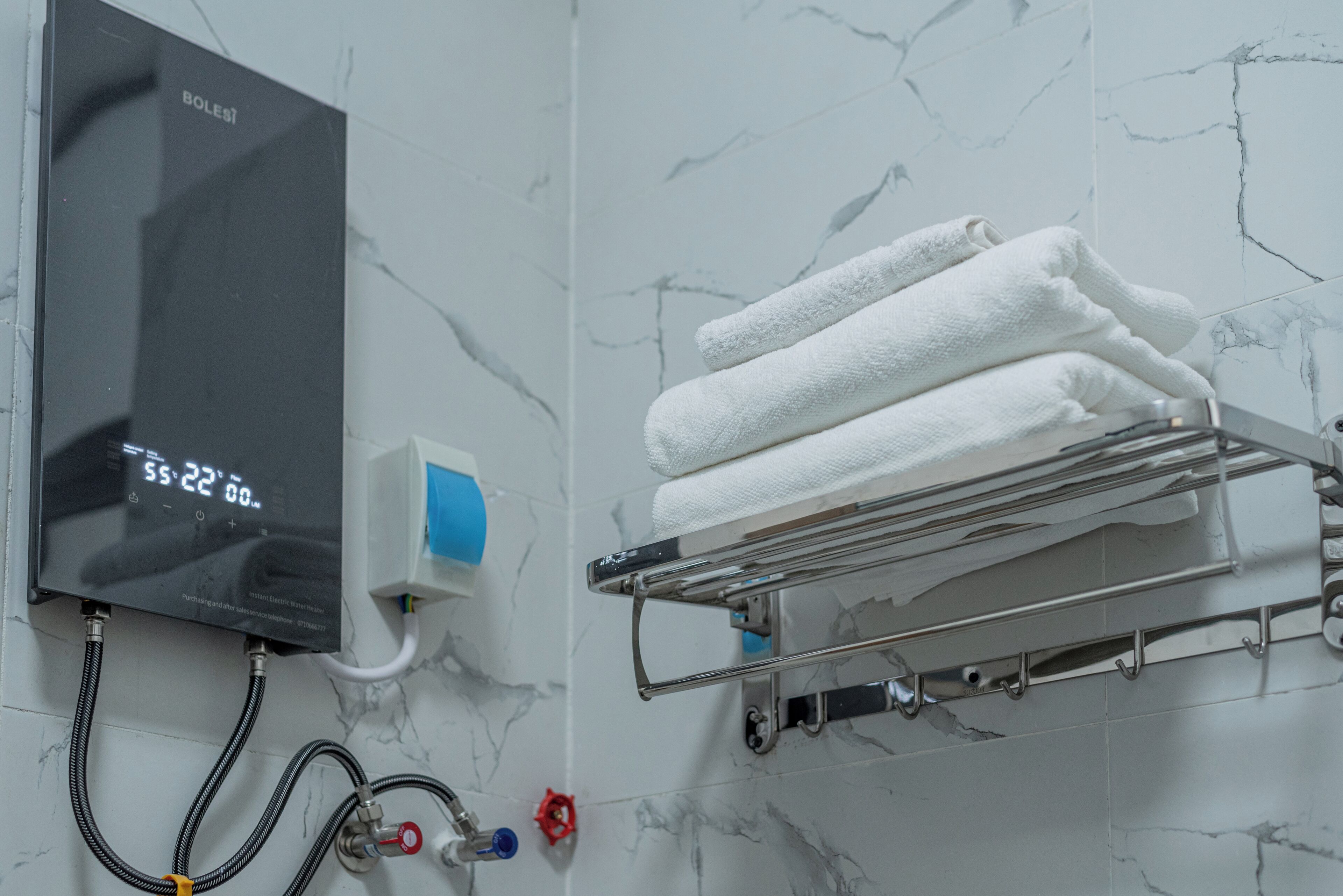 Ein Badezimmer mit Durchlauferhitzer, einem Handtuchhalter mit gefalteten Handtüchern und einer Wand mit Marmoroptik.