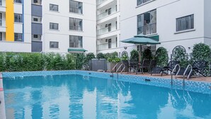 Una piscina amb vora enrajolada, envoltada per una zona de terrassa amb mobiliari exterior i un edifici al fons.