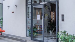 Entrada d'un edifici modern amb una porta de vidre, una tenda verda i plantes en testos.