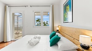 Una habitación de hotel con una cama, un cabecero de madera, una mesita de noche con una lámpara, un cuadro enmarco y vistas a través de un ventanal.