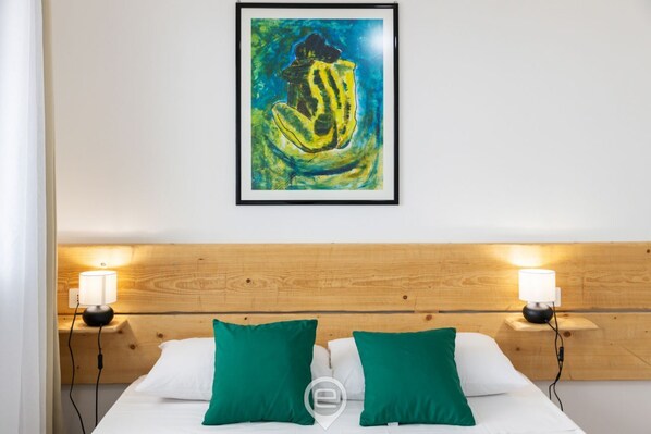 A bedroom with a wooden headboard, two bedside lamps, a framed painting, and two green pillows. - Sa Stadda - Camera Natura (Lanusei)