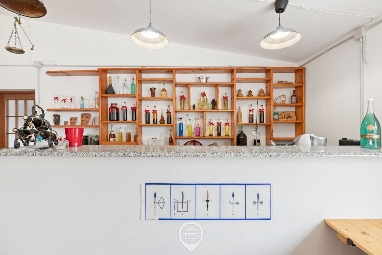 A bar area with wooden shelves displaying bottles and glasses, a scale, and a red cup.