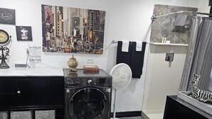 Une petite buanderie équipée d’un lave-linge, d’un ventilateur fixé au mur et d’un porte-serviettes.