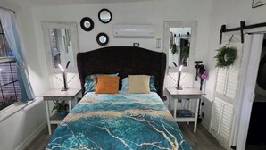 Une chambre à coucher avec un grand lit, deux tables de chevet, une fenêtre avec des rideaux et un climatiseur fixé au mur.