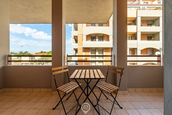Un balcon avec une table et des chaises en bois, donnant sur un immeuble d’habitation.