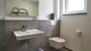 Ein Badezimmer mit einem weißen Waschbecken, einer Toilette, einem Spiegel und einem Fenster.