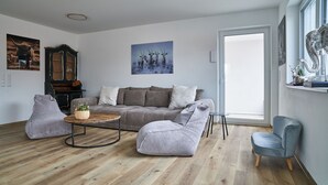 Ein modernes Wohnzimmer mit einer Couch, zwei Sesseln, einem Couchtisch und einem großen Fenster.