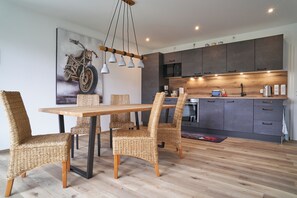Een moderne keuken met donkere kastjes, een houten eettafel, rieten stoelen en wanddecoratie met motorfietsmotieven.