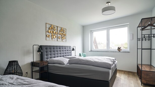 A bedroom with a large bed, a bedside table, a lamp, a wall art piece, a window, and a wooden shelf. - Vacation apartment Squirrel (Günzburg)